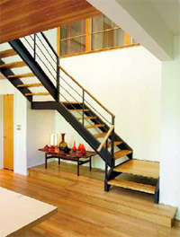 A steel beam buried in a wall secures a floating staircase from the foyer above. Open risers and oak-capped railings enhance the flow. White oak seems to spill down the stairs to the cedar-accented dining room and become another expanse of continuous flooring. The narrow door opens to a powder room.